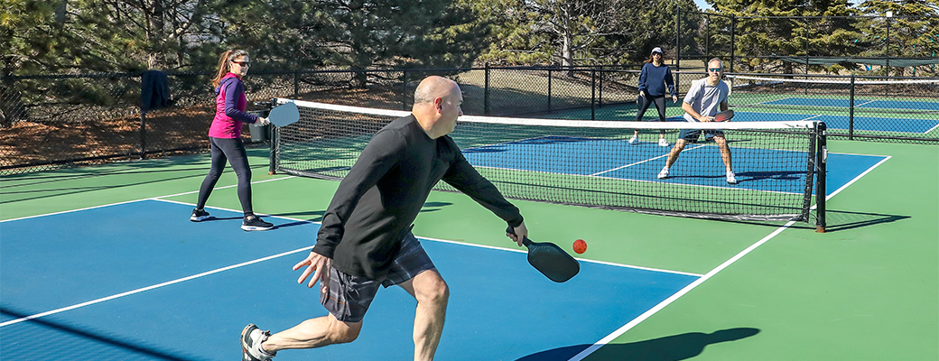 Image of middle-aged people playing pickleball outdoors on a pickleball court